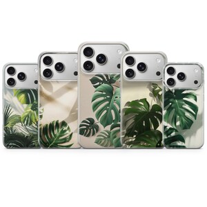 May include: Five clear phone cases with a tropical leaf design. The cases feature a variety of green monstera leaves and other tropical foliage against a neutral background. The phone cases are arranged in a row, showcasing the design.