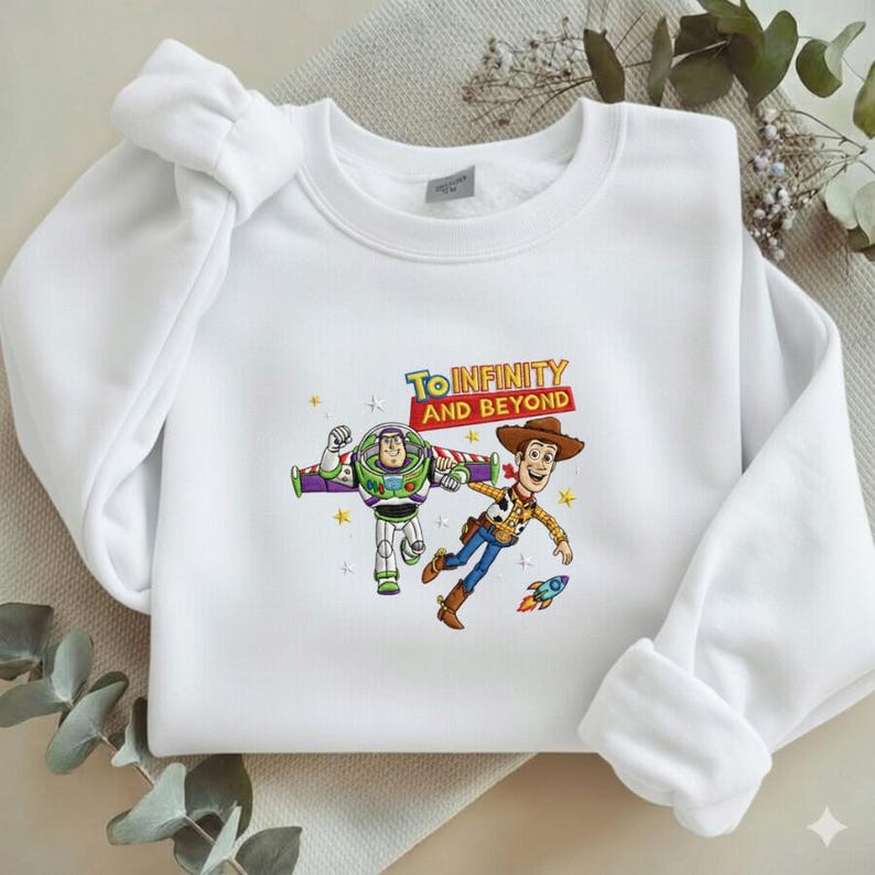 K&ouml;nnte beinhalten: Wei&szlig;es Sweatshirt mit Buzz Lightyear und Woody aus Toy Story, mit dem Text "TO INFINITY AND BEYOND". Die Grafik zeigt eine Rakete und Sterne. Das Sweatshirt hat einen Rundhalsausschnitt und lange &Auml;rmel.