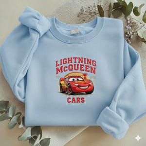 Puede incluir: Sudadera azul claro con un dise&ntilde;o de Lightning McQueen de la pel&iacute;cula Cars. El dise&ntilde;o incluye el texto "LIGHTNING MCQUEEN" y "CARS". La sudadera tiene mangas largas y cuello redondo.
