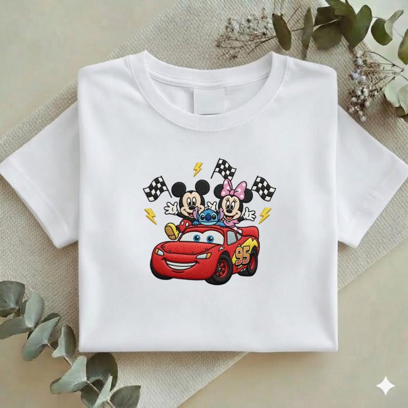 May include: White t-shirt featuring a colorful embroidered design. The design includes Mickey Mouse, Minnie Mouse, and Stitch riding in a red race car. Checkered flags and lightning bolts complete the racing theme.