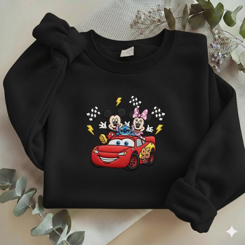 May include: Black sweatshirt featuring an embroidered design of Mickey Mouse, Minnie Mouse, Stitch, and Lightning McQueen from the Cars movie. The design includes racing flags and lightning bolts. The number 95 is on the car.