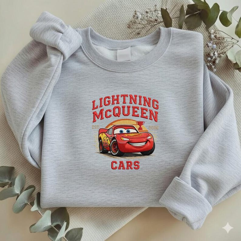 Puede incluir: Una sudadera gris claro con el texto "LIGHTNING McQUEEN" sobre una imagen de dibujos animados de un coche de carreras rojo. La palabra "CARS" est&aacute; impresa debajo. La sudadera tiene mangas largas.