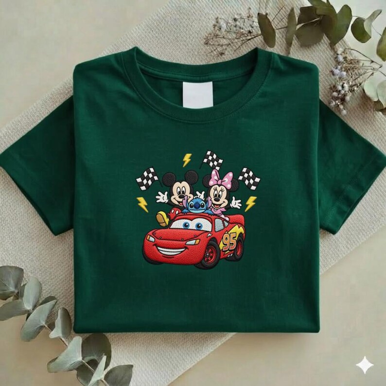 May include: Dark green t-shirt featuring an embroidered design of Mickey Mouse, Minnie Mouse, and Stitch riding in a red Lightning McQueen race car. The design includes checkered flags and lightning bolts.