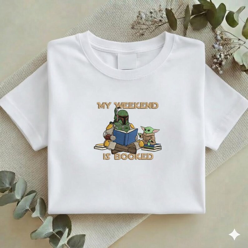 Pu&ograve; includere: T-shirt bianca con una grafica di un personaggio con un'armatura verde che legge un libro blu, con una piccola creatura verde. Il testo "MY WEEKEND IS BOOKED" &egrave; sopra e sotto i personaggi.