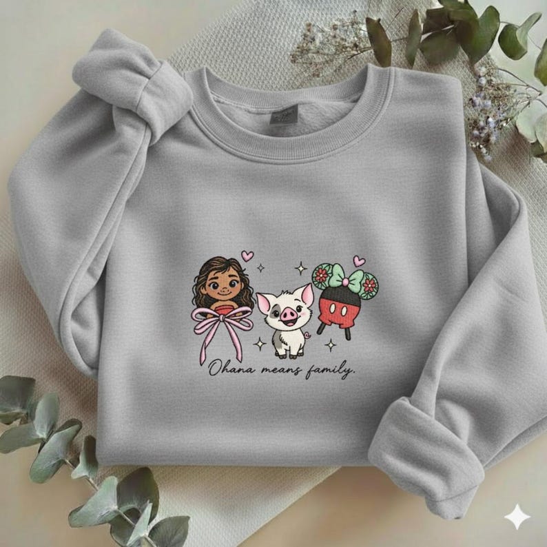 Puede incluir: Una sudadera gris claro con un dibujo animado de tres personajes: una ni&ntilde;a con un lazo rosa, un cerdo y un personaje inspirado en Mickey Mouse. La frase "Ohana means family" est&aacute; escrita debajo.
