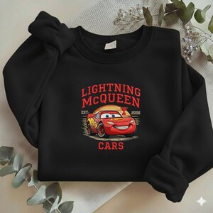 Puede incluir: Sudadera negra de cuello redondo con un dise&ntilde;o de Rayo McQueen de la pel&iacute;cula Cars. El dise&ntilde;o incluye el texto "LIGHTNING McQUEEN EST. 2006 CARS" en rojo y amarillo. La sudadera es de material suave.