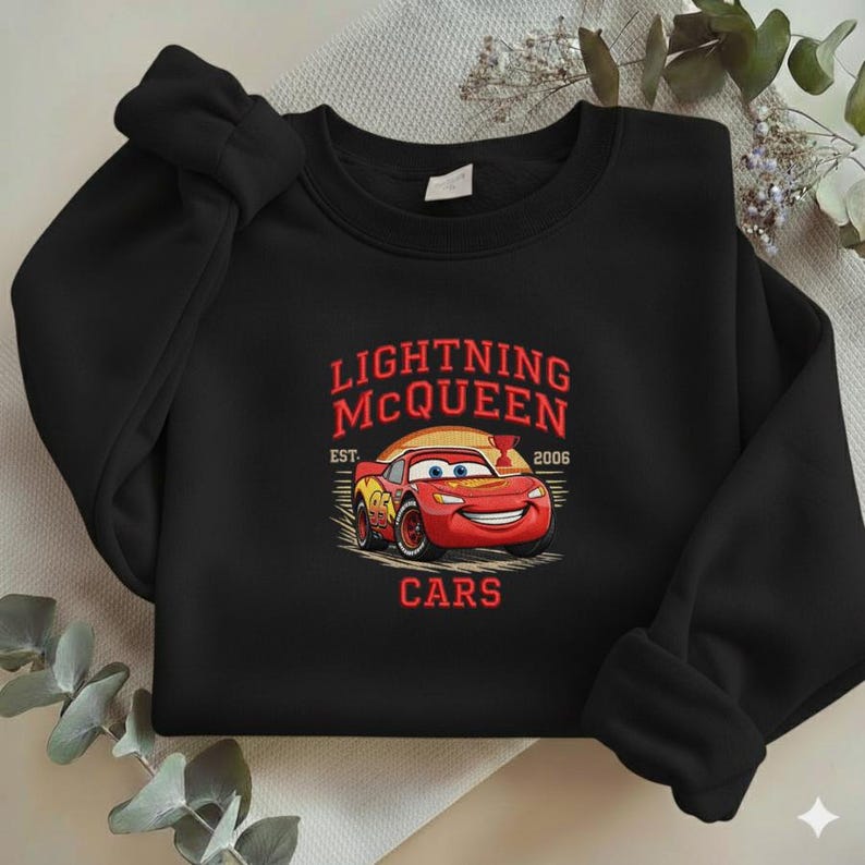 Puede incluir: Sudadera negra de cuello redondo con un dise&ntilde;o de Rayo McQueen de la pel&iacute;cula Cars. El dise&ntilde;o incluye el texto "LIGHTNING McQUEEN EST. 2006 CARS" en rojo y amarillo. La sudadera es de material suave.