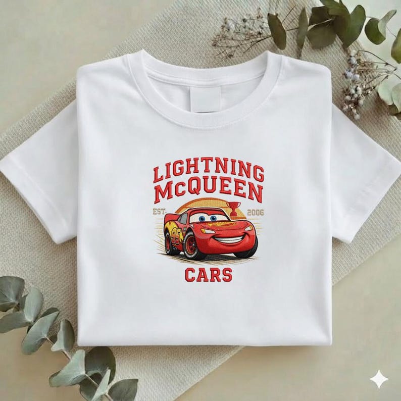 Puede incluir: Camiseta blanca con un dise&ntilde;o de Rayo McQueen de la pel&iacute;cula Cars. El dise&ntilde;o incluye el texto "LIGHTNING MCQUEEN" sobre un coche de carreras rojo sonriente, con "EST. 2006" y la palabra "CARS" debajo.