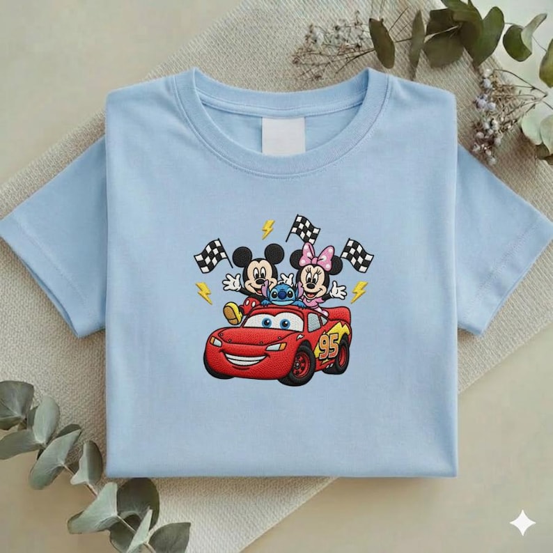 May include: Light blue t-shirt featuring an embroidered design of Mickey Mouse, Minnie Mouse, and Stitch riding in a red race car. The design includes checkered flags and lightning bolts. The car has the number 95 on the side.