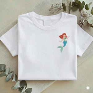 May include: A white ceramic mug with a black handle and the text "But First, Coffee" in a bold, black font. The mug is set against a blurred background, suggesting a cozy setting.