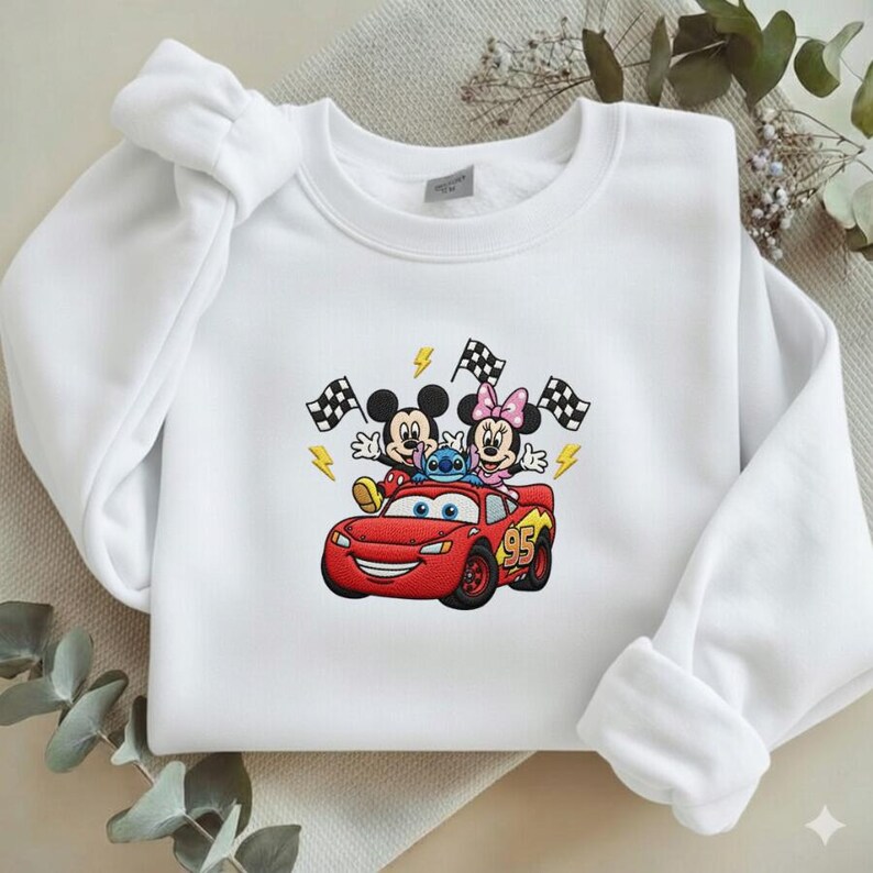 May include: White sweatshirt featuring an embroidered design of Mickey Mouse, Minnie Mouse, and Stitch riding in a red race car. The design includes checkered flags and lightning bolts. The car has the number 95 on the side.