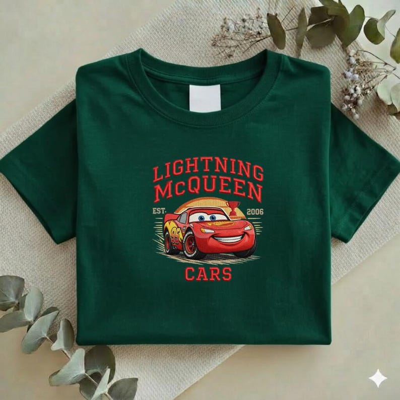 Puede incluir: Camiseta verde oscuro con un dise&ntilde;o de Rayo McQueen de la pel&iacute;cula Cars. El dise&ntilde;o incluye el texto "LIGHTNING McQUEEN" en rojo, con "EST. 2006" y la palabra "CARS" debajo del coche.