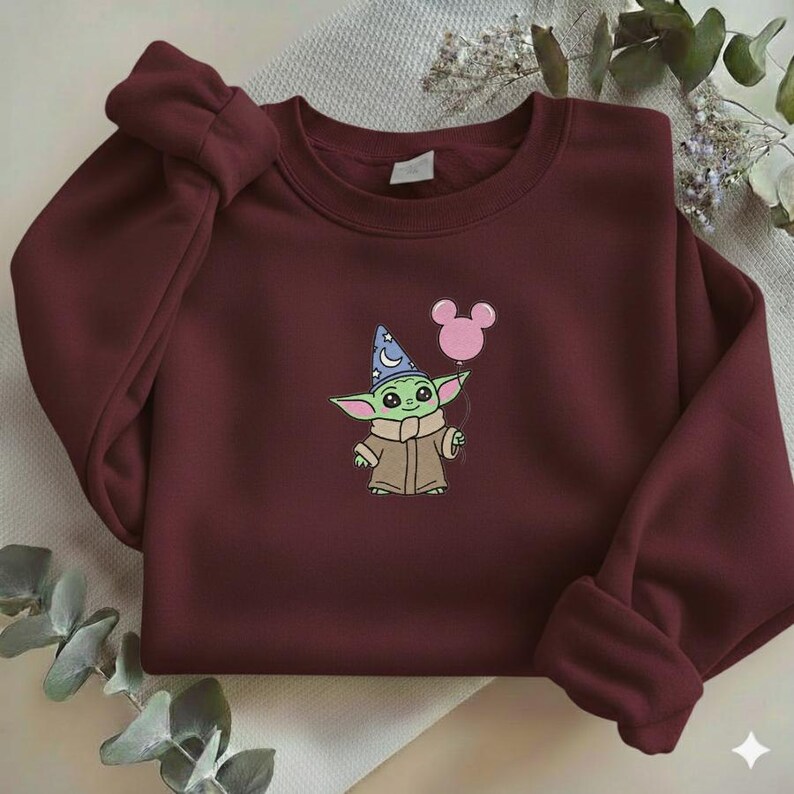 Op de afbeelding: Bordeaux sweatshirt met een geborduurd stripfiguur met een tovenaars hoed en een roze ballon. Het personage is groen met grote ogen en een bruine jas. De sweatshirt heeft een ronde hals en lange mouwen.