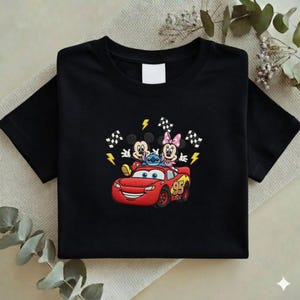 May include: Black t-shirt featuring an embroidered design of Mickey Mouse, Minnie Mouse, Stitch, and Lightning McQueen from the Cars movie. The design includes checkered flags and lightning bolts. The number 95 is on the car.
