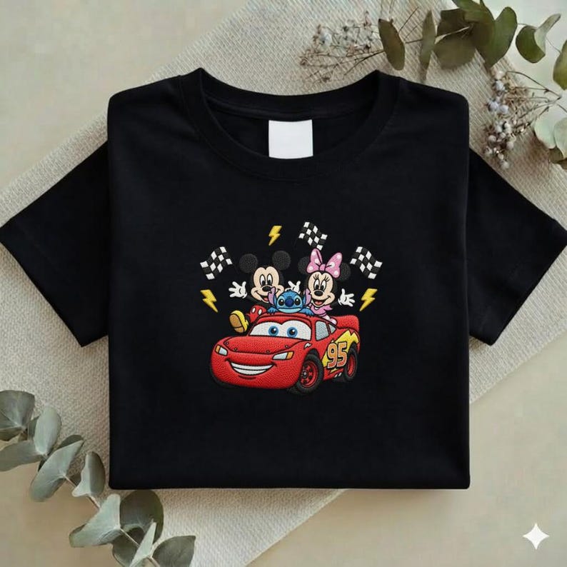May include: Black t-shirt featuring an embroidered design of Mickey Mouse, Minnie Mouse, Stitch, and Lightning McQueen from the Cars movie. The design includes checkered flags and lightning bolts. The number 95 is on the car.