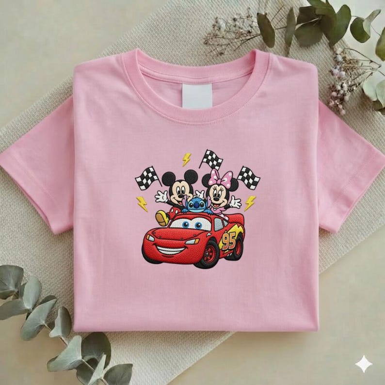 May include: Pink short-sleeved t-shirt featuring an embroidered design of Mickey Mouse, Minnie Mouse, Stitch, and Lightning McQueen. The design includes checkered flags and the number 95. The shirt is made of a soft material.