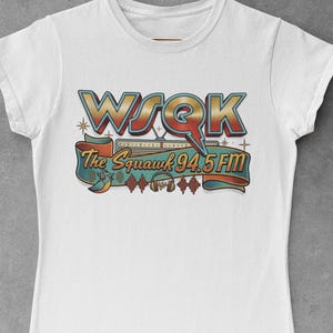 Könnte beinhalten: Weißes T-Shirt mit einem Retro-Design. Das Design zeigt den Text "WSQK The Squawk 94.5 FM", ein stilisiertes Radio, Noten und einen Vogel in Gold-, Blau- und Orangetönen.