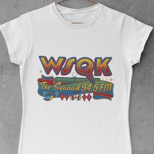 Könnte beinhalten: Weißes T-Shirt mit einem farbenfrohen Grafikdesign für WSOK The Squawk 94.5 FM. Das Design umfasst die Funkrufzeichen, ein Banner mit dem Namen des Senders und Radiowellen-Symbole. Das Shirt ist aus weichem Material.