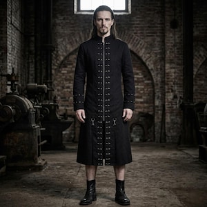 May include: A long black coat with a high collar and metal detailing. The coat has a zip fastening and decorative metal hardware down the front and on the sleeves. The knee-length coat is worn with black boots. The background is an industrial space with brick walls.