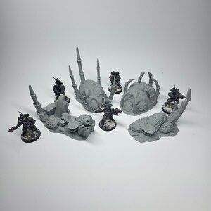May include: A tabletop gaming scene featuring miniature figures and terrain. The scene includes several gray, textured terrain pieces and multiple painted miniature figures. The figures are in various poses, suggesting action. The overall aesthetic is reminiscent of a science fiction or fantasy setting.