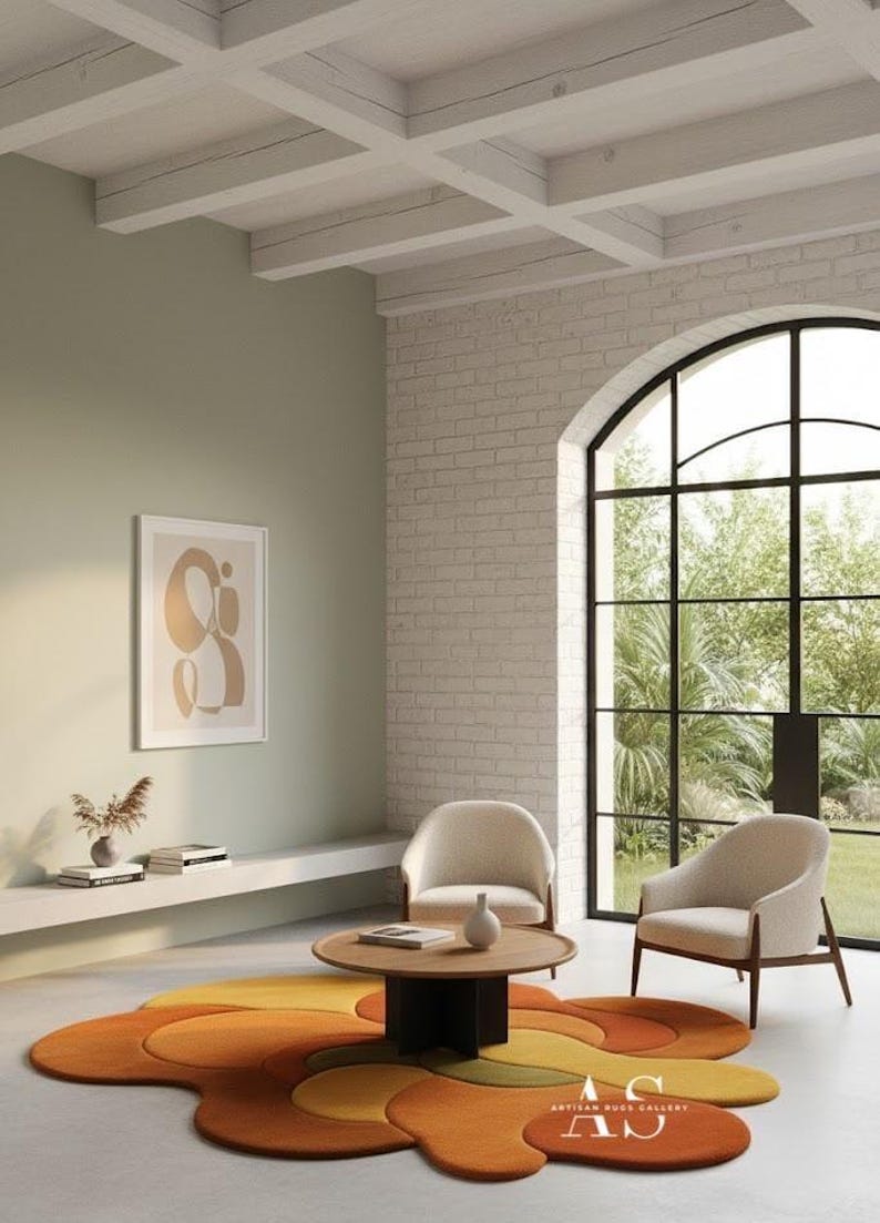 Puede incluir: Un sal&oacute;n moderno con una colorida alfombra abstracta en tonos naranja, amarillo y verde. Dos sillones color crema frente a una mesa de centro redonda de madera. Una obra de arte enmarcada y una gran ventana completan el elegante interior.
