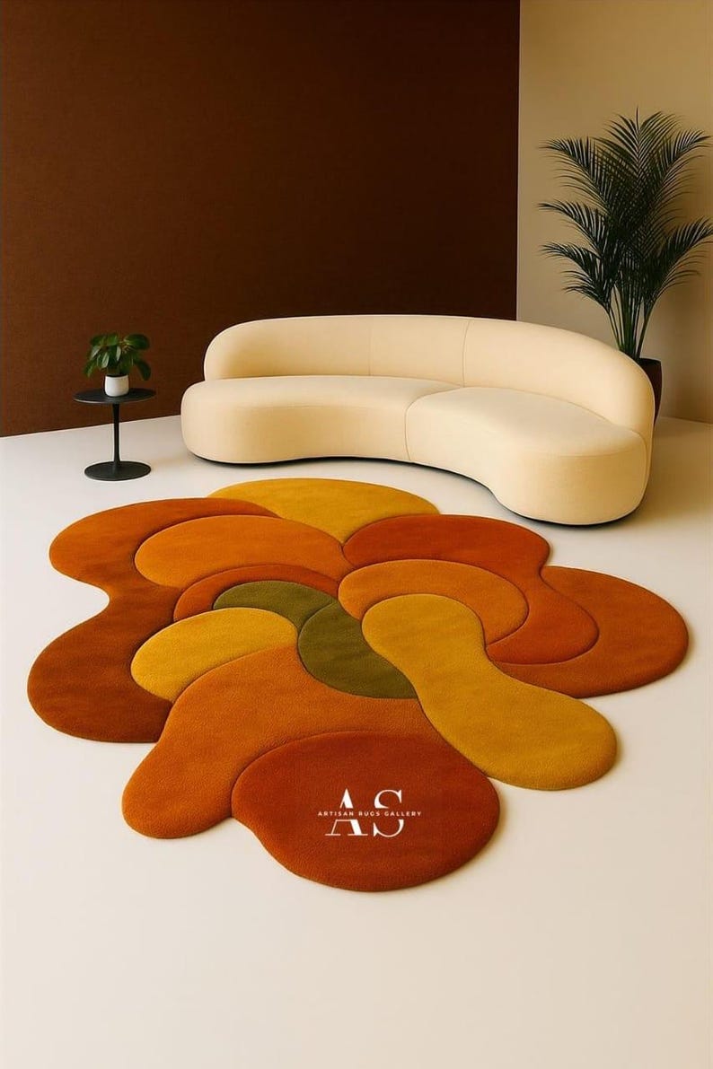 Puede incluir: Una alfombra abstracta en tonos naranja, amarillo y verde, con un dise&ntilde;o fluido. Un sof&aacute; curvo de color crema est&aacute; en el fondo. La alfombra est&aacute; sobre un suelo blanco. Las palabras "ARTISAN RUGS GALLERY" est&aacute;n impresas en la alfombra.