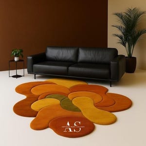 Puede incluir: Un sal&oacute;n moderno con un sof&aacute; de cuero negro y una alfombra abstracta y colorida. La alfombra tiene un dise&ntilde;o floral con tonos de naranja, amarillo y verde. La alfombra tiene el texto "AS ARTISAN RUGS GALLERY".