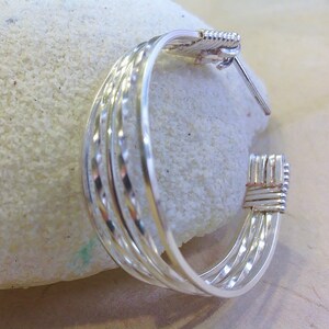 May include: Silver hoop earrings with a woven design. The earrings are made of multiple strands of silver wire that are woven together to create a unique and stylish look.