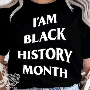 May include: Black t-shirt with the white text "I AM BLACK HISTORY MONTH". The shirt also features the logo "Thunder Hoofs Studio" at the bottom left. The shirt is a crew neck style.