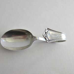 May include: A silver baby spoon with a loop handle. The handle is engraved with the name "Alice".
