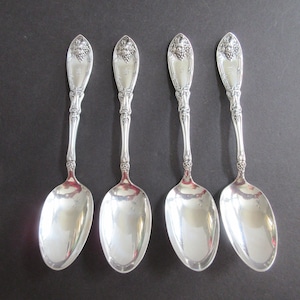 May include: Set of four silver spoons with ornate handles featuring a grape motif. The spoons have a polished finish and are in excellent condition.