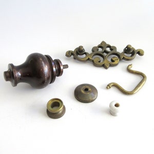 May include: Assortment of vintage cabinet hardware, including a brown wooden knob, a brass pull, a brass escutcheon, a brass knob, and a white porcelain knob.