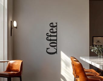 May include: A black metal wall art piece spelling the word "Coffee" in a vertical orientation. The sign is mounted on a light-colored wall. The image also shows brown leather chairs and a marble countertop.