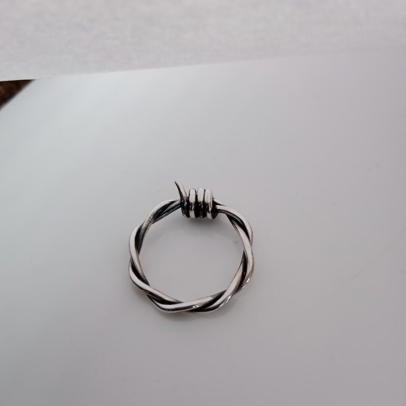 Pu&ograve; includere: Un anello color argento con un design a filo spinato. L'anello &egrave; circolare, con il filo attorcigliato su se stesso per formare la fascia. La parte superiore dell'anello presenta una piccola sezione del filo avvolto per assomigliare a delle spine.