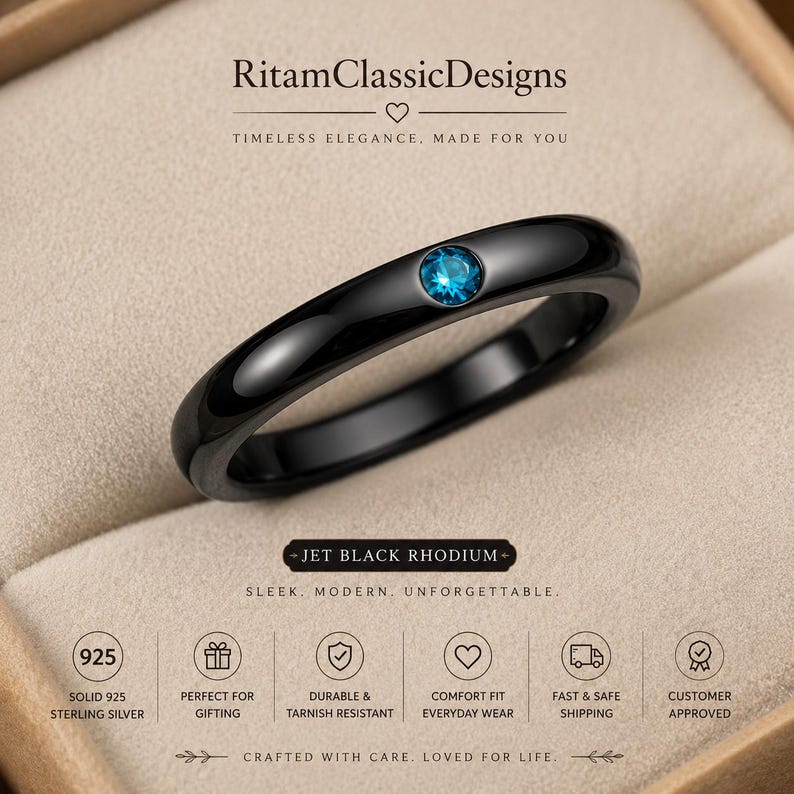 May include: A polished jet black rhodium ring featuring a single round brilliant-cut blue gemstone set in the centre. The band has a smooth, rounded profile. Text on the image includes RitamClassicDesigns, Jet Black Rhodium, and 925 Solid Sterling Silver.