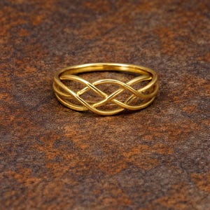 May include: A gold ring with a woven design. The ring has an intricate pattern of interwoven strands, creating a textured and visually appealing aesthetic. The ring is a piece of jewellery.