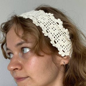 Peut inclure: Bandeau en crochet de couleur crème avec un bord festonné. Le bandeau est porté sur la tête. L'image montre un gros plan du bandeau et de la personne qui le porte. La personne porte également un collier de perles et un haut blanc.