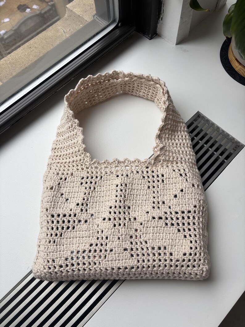 K&ouml;nnte beinhalten: Beige, handgeh&auml;kelte Tragetasche mit einem wellenf&ouml;rmigen oberen Rand. Die Tasche hat ein offenes Design, das ihr ein strukturiertes Aussehen verleiht. Die Tasche ist zum Tragen &uuml;ber der Schulter konzipiert.
