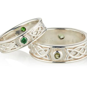 Two Sterling Silver Irish made Claddagh bands, one large and one small. There is a Celtic design around the band and two small gemstones in bezel settings at the halfway points around the bands. Two plain rims border the band.