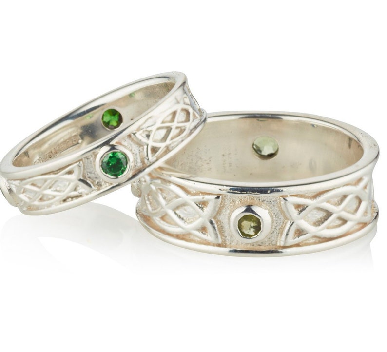 Two Sterling Silver Irish made Claddagh bands, one large and one small. There is a Celtic design around the band and two small gemstones in bezel settings at the halfway points around the bands. Two plain rims border the band.