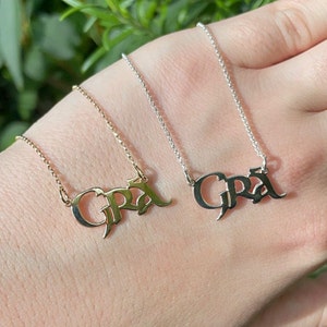 Könnte beinhalten: Zwei Halsketten, eine goldene und eine silberne, mit dem Namen "Gra" in gotischer Schrift.