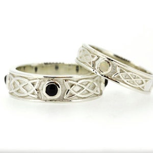 May include: Two silver Celtic knot wedding bands. One band features black gemstones and the other has a white gemstone.
