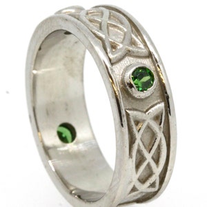 May include: A silver Celtic knot band ring with two green gemstones. The ring is a classic design with a detailed knot pattern.