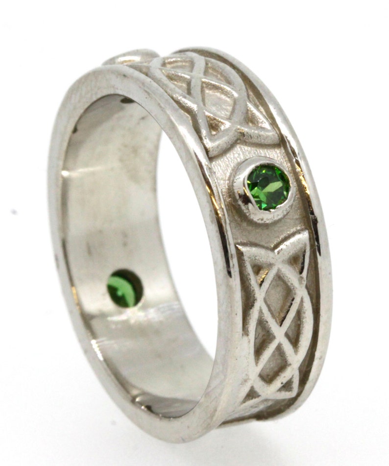 May include: A silver Celtic knot band ring with two green gemstones. The ring is a classic design with a detailed knot pattern.