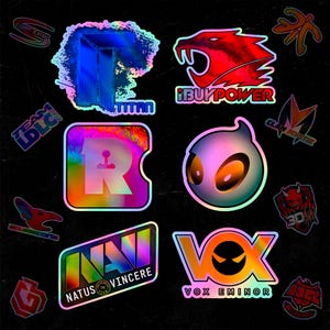 May include: A collection of holographic gaming team stickers featuring various logos including Titan, iBUYPOWER, Team LDLC, Clan Mystik, 3DMAX, Natus Vincere, and Vox Eminor. The stickers display vibrant, shifting colors and metallic finishes.