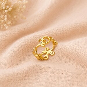 May include: A gold-toned ring featuring an openwork design with repeating swirling vine and leaf motifs. The band is constructed from interconnected metal segments that form a continuous pattern of organic, curved shapes around the circumference.