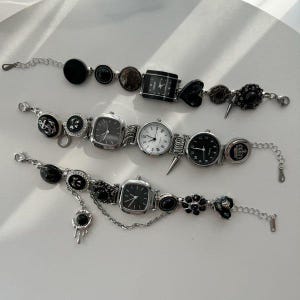 Puede incluir: Tres pulseras de reloj únicas con varias esferas y elementos decorativos. Las pulseras presentan tonos negros, plateados y grises, con adornos como corazones, púas y diseños florales. Los relojes tienen esferas cuadradas y redondas.