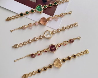 May include: Five gold-toned wristwatches with various face shapes, including hearts and squares. The watch faces are in shades of green, pink, white, red, and gold. The bands feature decorative elements like pearls, flowers, and gemstones.