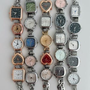 May include: Five vertical rows of linked wristwatches featuring various case shapes including square, round, and heart-shaped designs. The watches display diverse dial colors such as black, white, pink, blue, and green, with silver and rose gold metal finishes.