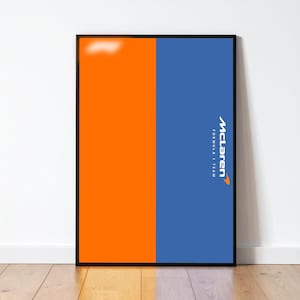 May include: A framed poster with a vertical split design. One side is bright orange, the other is blue. The McLaren Formula 1 Team logo is displayed in white on the blue side. The frame is black.